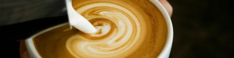Barista vertiendo leche espumosa en una taza de café, creando un arte latte con un diseño en espiral.